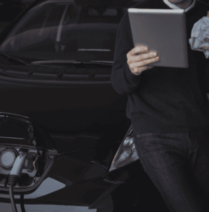 Man using a digital tablet while charging an electric car, symbolizing advanced power battery solutions